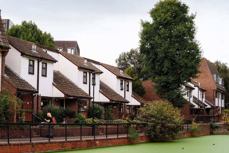 Photograph of a residential building situated along the edge of a canal in Haggerston, E2. The building is constructed of red brick with multiple balconies and large windows, some of which are open. I